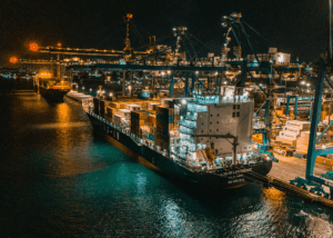 Navio Log-In Experience atracado à noite em terminal portuário, durante operação de cabotagem no Brasil, com guindastes movimentando contêineres para garantir agilidade, segurança e eficiência logística.